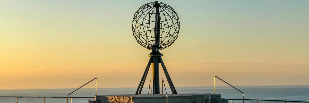 Das ikonische Nordkap-Monument mit dem eisernen Globus vor einem goldenen Sonnenuntergang über dem Nordmeer, ein Highlight jeder Norwegen-Kreuzfahrt.