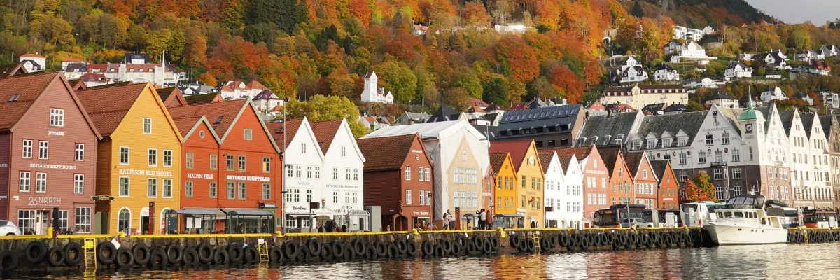 Bunte Häuser am Ufer in Bergen im Hebst mit rotbraunen Bäumen im Hintergrund.