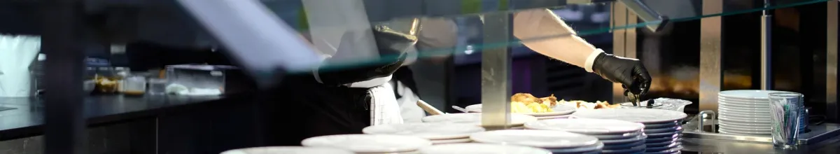 Ein Mann mit Handschuhen bereitet das Abendbuffet bei Hurtigruten vor. Eine Reihe von Tellern steht für die Gäste bereit.