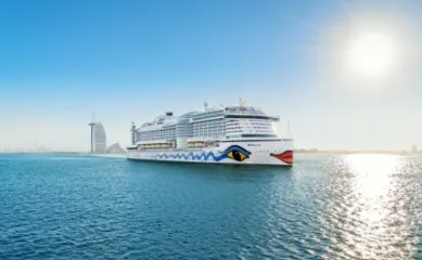 Das Kreuzfahrtschiff AIDAprima gleitet im tiefblauen Wasser, im Hintergrund ist Burj Al Arab im Dubai zu sehen.