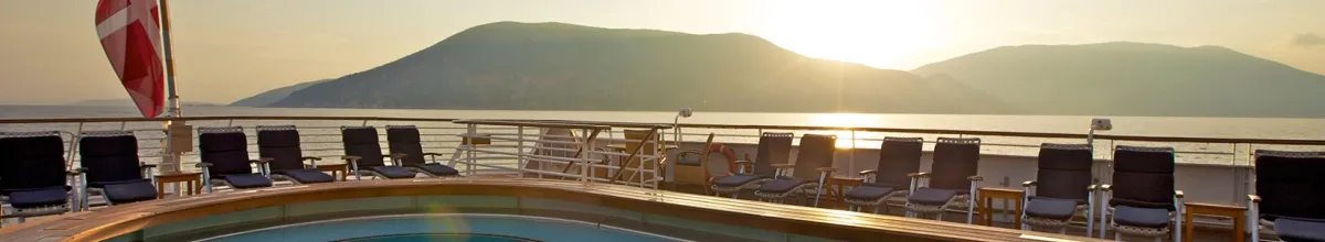 Der Außenpool auf den SeaDream Yachten mit Liegestühlen. Eine hügelige Landschaft liegt im Hintergrund und die Sonne geht zwischen zwei Felsen unter.