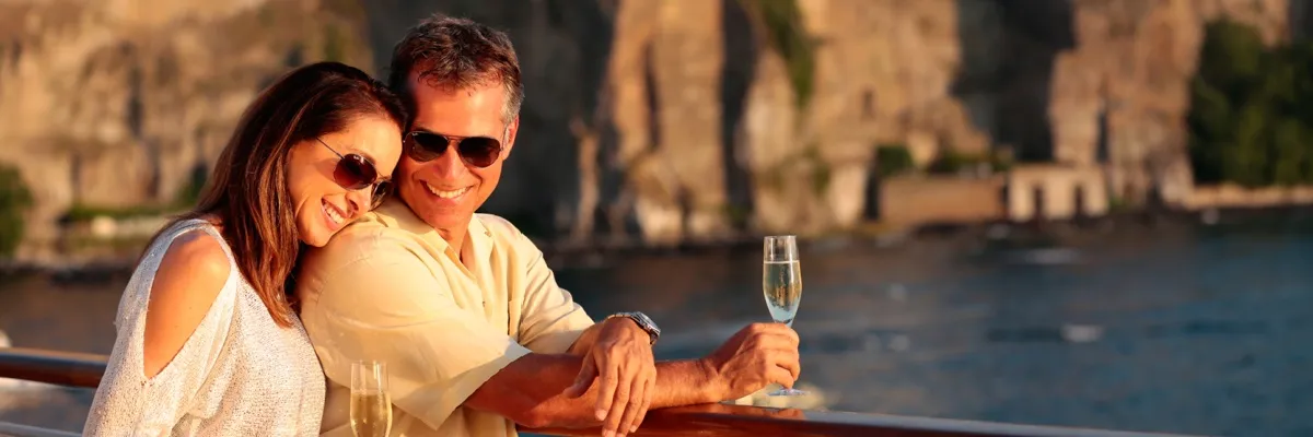 Ein Pärchen an Deck einer SeaDream Yacht mit Sektgläsern in der Hand im Sonnenuntergang.