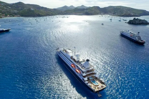 Die SeaDream I und SeaDream II vor einer felsigen Küste an einem sonnigen Tag.