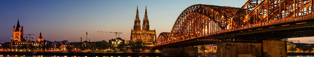 Panorama der Kölner Skyline bei Dämmerung mit dem beleuchteten Dom und der Hohenzollernbrücke – der Standort von Ahoi-Schiff.de, dem fairsten Kreuzfahrtportal Deutschlands.