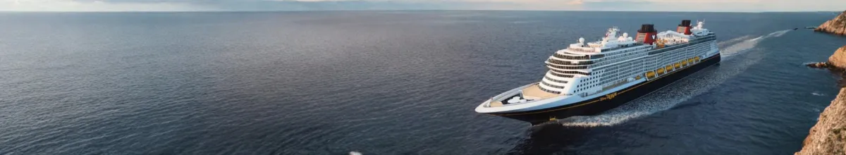 Die Schiffe der Disney Cruise Line Die Disney Treasure im Mittelmeer fährt vorbei an einer steinigen Klippe. Der Horizont erstreckt sich im Hintergrund.