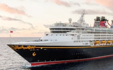 Die Disney Magic auf offener See. Die Wolken am Himmel werden durch den Sonnenuntergang in sanftes Licht getaucht. ©Disney