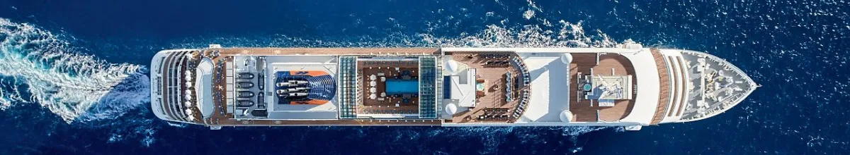 Eine beeindruckende Luftaufnahme der EUROPA 2 auf offener See. Die Draufsicht zeigt die weitläufigen Decks, den Poolbereich und die weiße Heckwelle des Luxusschiffes im Kontrast zum tiefblauen Wasser des Mittelmeers.