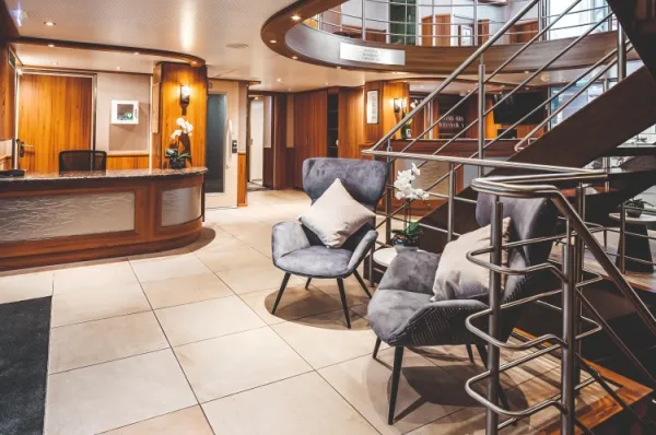 MS Swiss Pearl Rezeption Rezeptionsbereich an Bord der MS Swiss Pearl mit zwei Sesseln, im Hintergrund führt eine Treppe ins Oberdeck.