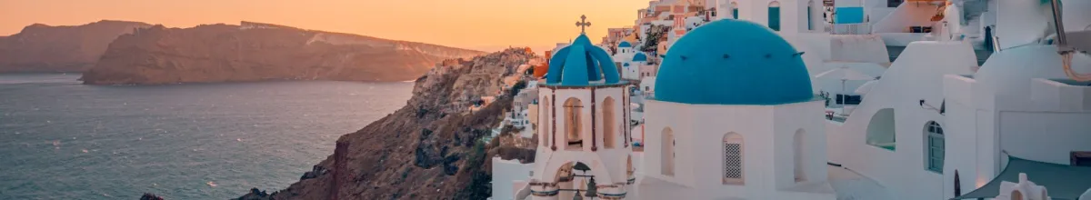 Die Stadt Santorini mit den weißen Häusern und blauen Dächern im Sonnenuntergang.