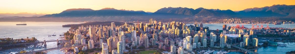 Die Skyline von Vancouver aus der Vogelperspektive aufgenommen mit der Sonne, die hinter der bergigen Landschaft untergeht.
