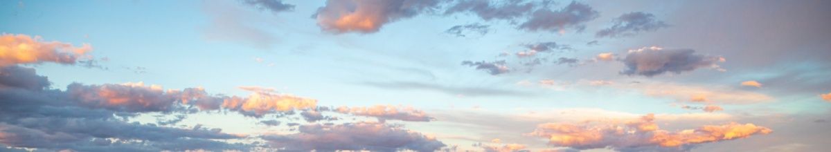 Flockige Wolken am Himmel im Sonnenaufgang in hellblau und korallefarbenen Lichtern.