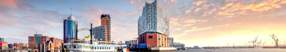 Die Elbphilharmonie Hamburg direkt an der Elbe bei einem wolkigen Sonnenuntergang im Panorama-Format.