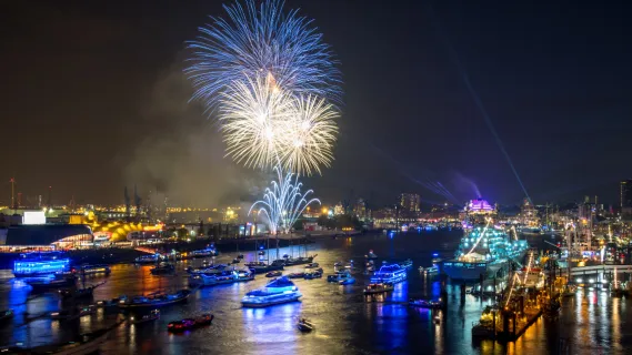 Nächtliche Schiffsparade im Hamburger Hafen mit einem bunten Feuerwerk im Hintergrund.