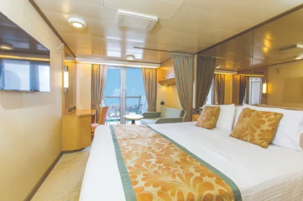 Die Deluxe-Balkonkabine an Bord von P&O Cruises mit einem Doppelbett, Spiegel und einer großen Balkon-Tür. Eingerichtet ist das Zimmer mit goldenen Akzenten.