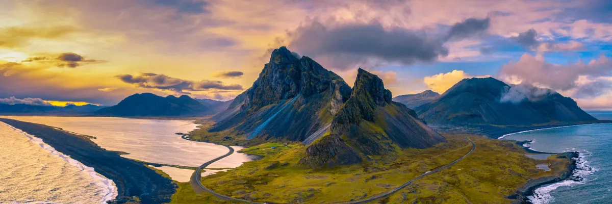 Abenteuer im hohen Norden: Island-Rundreisen im Sommer 2028 entdecken Die dramatische Bergkulisse des Vestrahorn in Island mit schwarzen Sandstränden und einer kurvigen Küstenstraße bei Sonnenuntergang – ein Ziel der AIDA Nordeuropa-Routen 2028.