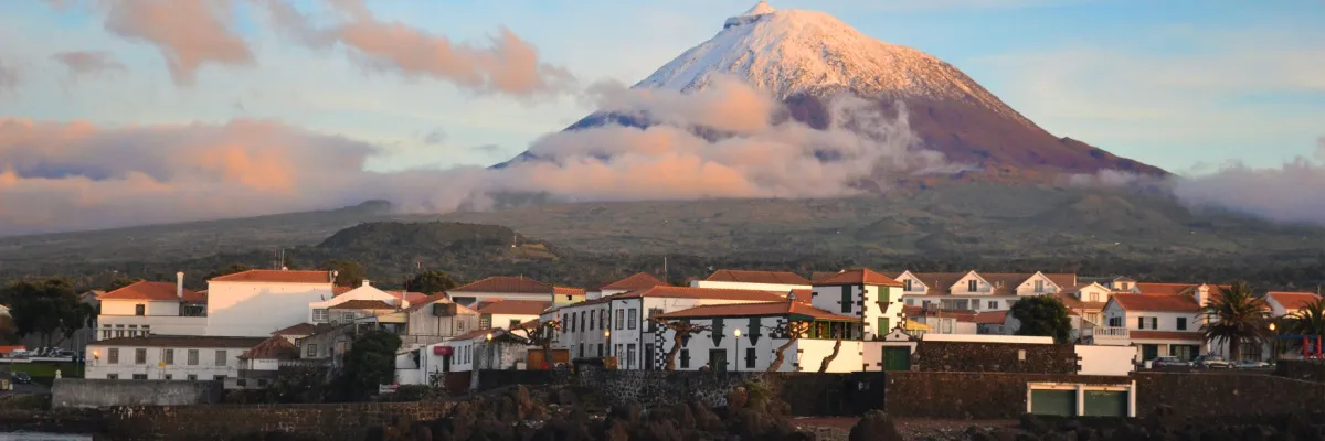 AIDA Azoren 2027: Spektakuläre Ausblicke auf den Vulkan Pico genießen Traditionelle weiße Häuser auf den Azoren mit dem schneebedeckten Vulkan Pico im Hintergrund, ein Highlight der AIDA Reisen 2027.