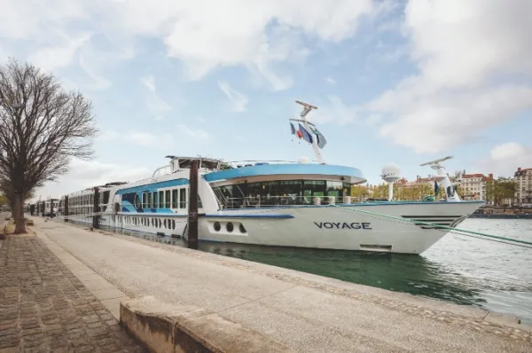 Die MS Voyage am Anleger am Ufer eines Flusses bei schönem Wetter und einer menschenleeren Promenade.