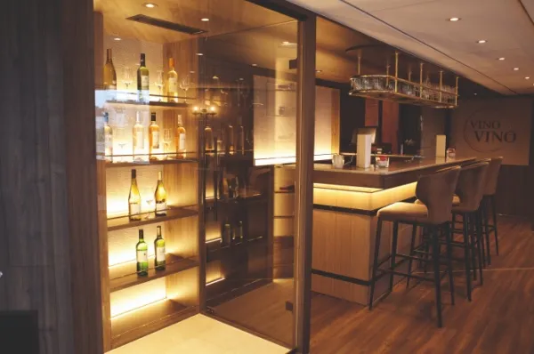Eine Bar mit Barhockern, gemütlicher Beleuchtung und einem Weinregal an Bord der MS Voyage.
