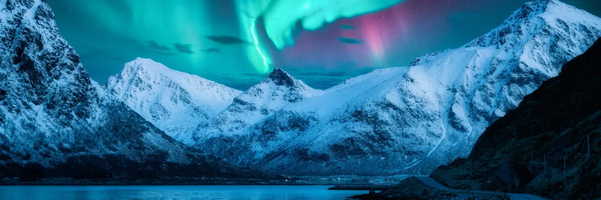 Spektakuläre grüne Polarlichter über schneebedeckten Bergen in Norwegen – ein Highlight der AIDA Nordeuropa Kreuzfahrten.
