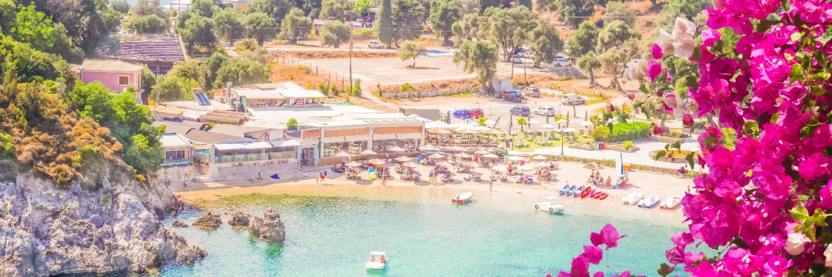 Blick auf eine idyllische Badebucht mit türkisblauem Wasser und leuchtend pinken Bougainvillea-Blumen – typisches Flair der griechischen Inseln.