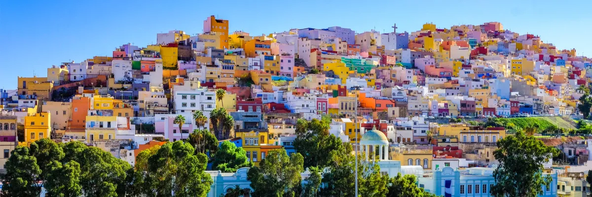 Dicht gestaffelte, farbenfrohe Häuserfassaden an einem sonnigen Hang in Las Palmas de Gran Canaria unter strahlend blauem Himmel – ein lebendiges Zeugnis kanarischer Architektur während einer Reise mit AIDAprima.
