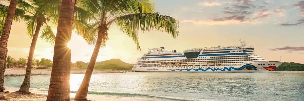 AIDAluna vor einer tropischen Küste mit Palmen zur Bewerbung der AIDA Internet-Aktion für Karibik-Kreuzfahrten 2026.
