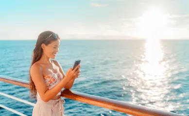 AIDA Internet-Aktion 2026 – Kostenfrei vernetzt auf Fernreisen Frau nutzt Smartphone auf AIDA Kreuzfahrt an Deck bei Sonnenuntergang für die gratis Internet-Flat 2026.