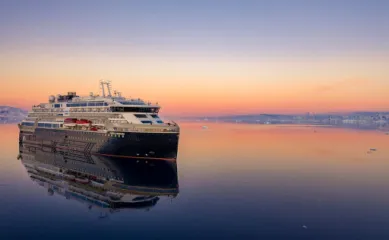 Modernes HX Expeditionsschiff spiegelt sich im ruhigen Polarmeer bei Sonnenuntergang anlässlich des 130-jährigen Jubiläums von Hurtigruten Expeditions.