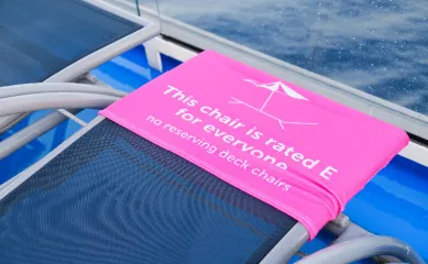 Pinkes Hinweisschild gegen das Reservieren von Sonnenliegen auf einem Kreuzfahrtschiff – Kreuzfahrt-Knigge.
