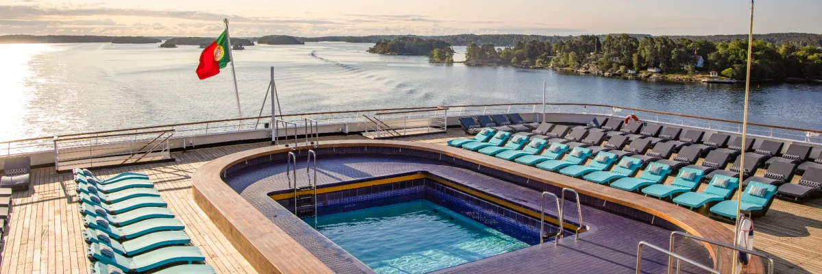 Das einladende Sonnendeck der VASCO DA GAMA von nicko cruises mit Pool und zahlreichen blauen Liegestühlen vor einer malerischen Inselkulisse als Illustration für die mychoice Duo-Deal Angebote 2026.