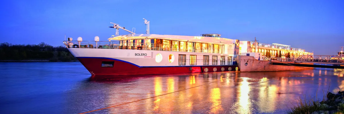 Das festlich beleuchtete Flussschiff BOLERO von nicko cruises spiegelt sich zur blauen Stunde im ruhigen Wasser eines Flussufers passend zu den Duo-Deal Angeboten 2026.