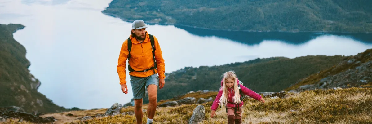 Vater und Tochter wandern in der norwegischen Gebirgslandschaft mit Blick auf einen tiefblauen Fjord – aktive Naturerlebnisse im Nordland-Winter 2026/27 mit der <em>Mein Schiff Flow</em>.