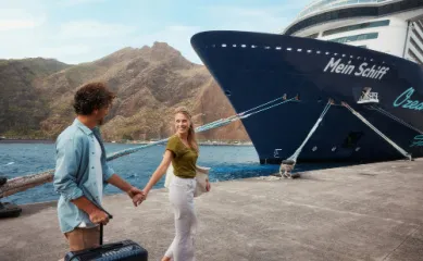 Ein lächelndes Paar geht am Hafen auf ein Schiff der TUI Cruises Flotte zu – ideal für die Planung der <em>Mein Schiff Flow</em> Winterkreuzfahrt 2026/27 mit bis zu 250 Euro Frühbucher-Ermäßigung.