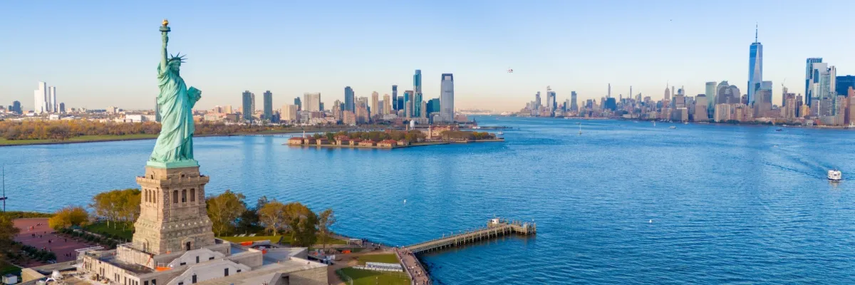 Blick über den Hafen von New York mit der Freiheitsstatue vorne links und der Skyline der Stadt im Hintergrund.