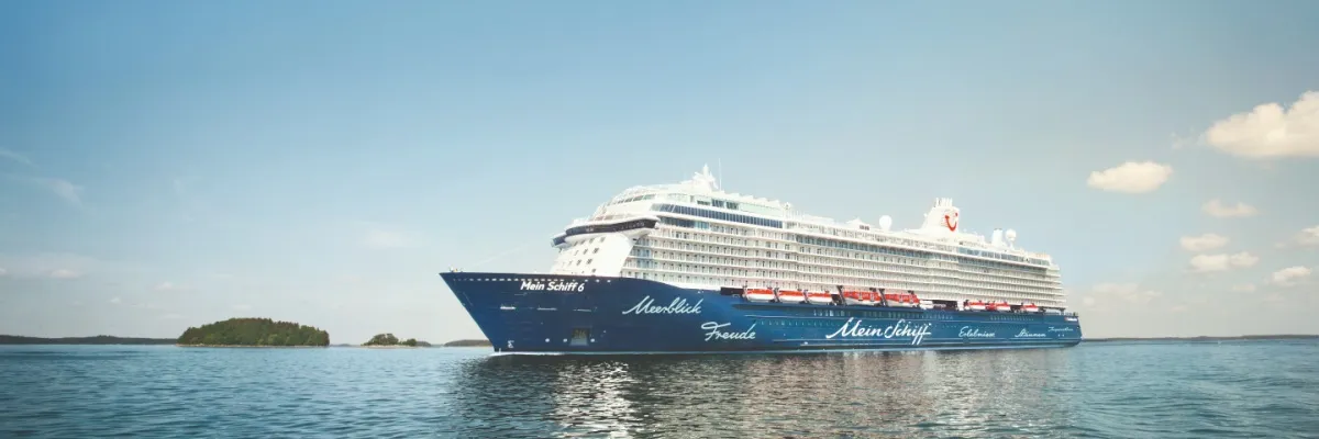 Seitenansicht von Mein Schiff 6 auf dem Meer. Im Hintergrund ist eine kleine Inselgruppe zu sehen.