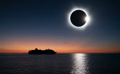Kreuzfahrtschiff als Silhouette auf ruhiger See unter einer totalen Sonnenfinsternis mit Korona und Diamantring am Abendhimmel.