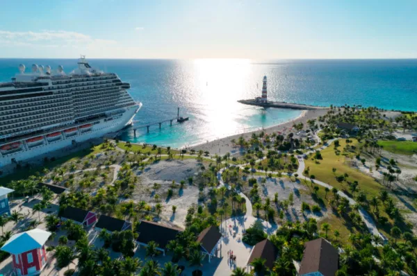 Ein großes MSC Cruises Kreuzfahrtschiff angelegt an der Privatinsel Ocean Cay MSC Marine Reserve auf den Bahamas mit weißem Sandstrand und dem markanten rot-weiß gestreiften Leuchtturm.