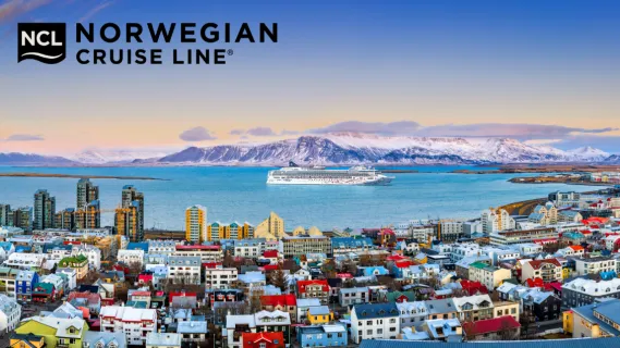 Die Norwegian Star im Hafen von Reykjavik. Vorne die farbenfrohen Häuser der Stadt, mittig das Schiff im Nordmeer, dahinter schneebedeckte Felsen.