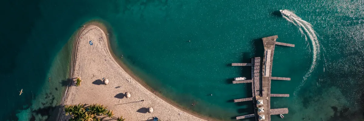Harvest Caye von oben – Strand und Jachthafen im Luftbild Luftaufnahme der tropischen Landzunge von Harvest Caye mit weißem Sandstrand, Palmen und dem hölzernen Bootssteg im türkisfarbenen Wasser von Belize.