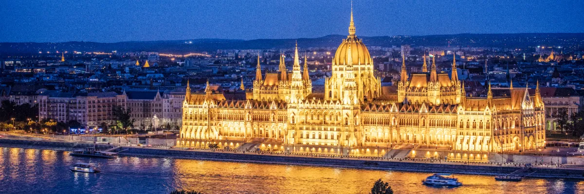 Das festlich beleuchtete Parlamentsgebäude in Budapest an der winterlichen Donau Das prachtvoll golden illuminierte ungarische Parlamentsgebäude in Budapest bei Nacht, direkt am Ufer der Donau mit vorbeifahrenden Schiffen während einer winterlichen Flusskreuzfahrt.