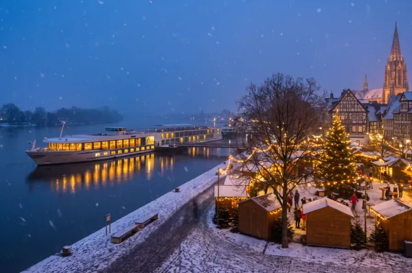 Adventskreuzfahrt – Flussschiff am Weihnachtsmarkt Adventskreuzfahrt auf dem Rhein – Flussschiff am beleuchteten Weihnachtsmarkt einer Altstadt im Schnee