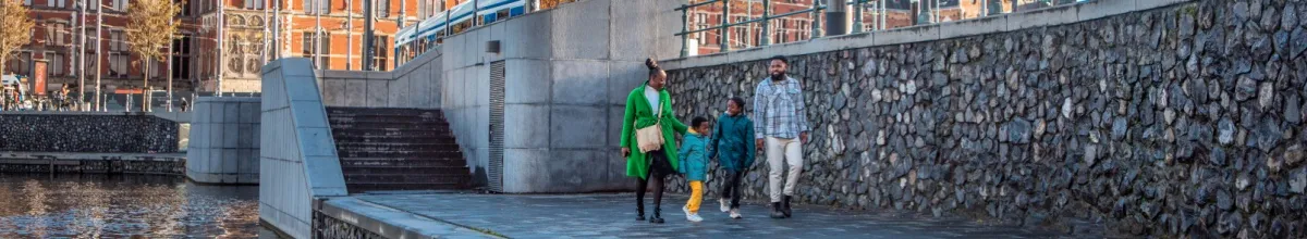 Eine vierköpfige Familie spaziert entspannt an einem Kanal in Amsterdam entlang.