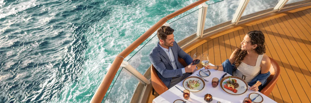 NCL Lifestyle-Flotte: Erstklassiges Dining unter freiem Himmel Ein Paar genießt ein exquisites Abendessen mit Wein und Meerblick auf dem weitläufigen Außendeck der Norwegian Cruise Line Lifestyle-Flotte.