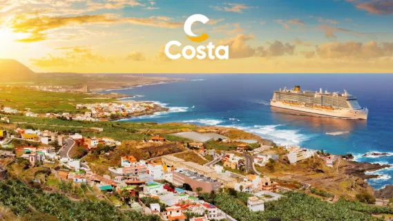 Blick aus der Vogelperspektive auf ein Costa Schiff vor der Küste einer Kanareninsel. Links im Hintergrund ist die untergehende Sonne zu sehen, mittig oben das Costa Logo in weiß und gelb.