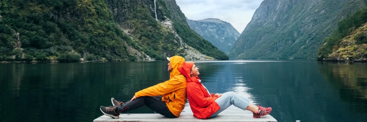 AIDA Last Minute 2026: Die spektakuläre Natur Norwegens und skandinavische Highlights hautnah erleben Ein Paar genießt in Outdoor-Kleidung die Stille an einem norwegischen Fjord während einer AIDA Last Minute 2026 Kreuzfahrt durch Nordeuropa.