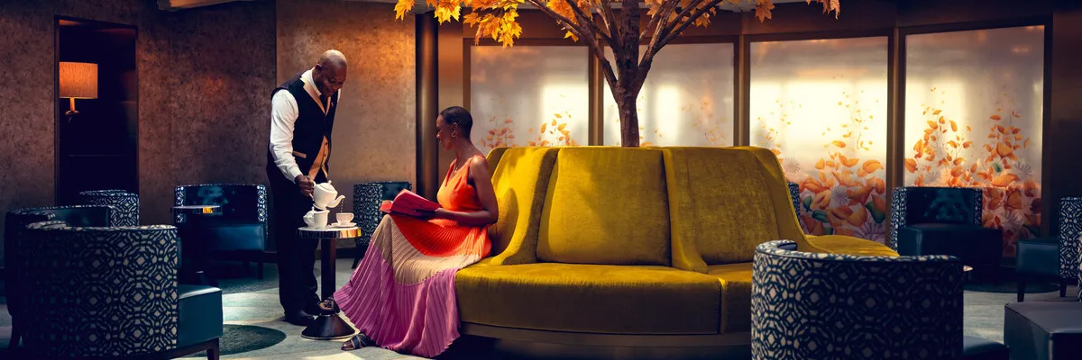 Cunard Bordleben – Exklusiver Service und entspannte Momente an Bord Eine Gästin genießt den aufmerksamen White Star Service™ in einer stilvollen Lounge an Bord eines Cunard Schiffes.