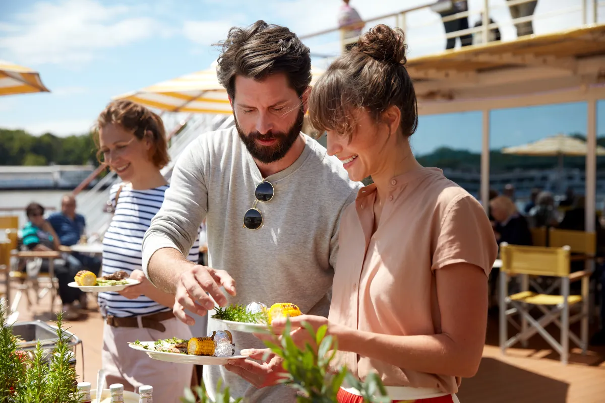 Gäste genießen ein frisches BBQ-Buffet auf dem sonnenverwöhnten Deck einer A-ROSA Flusskreuzfahrt.