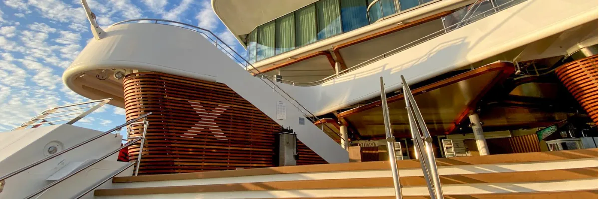 Modern Luxury Architektur an Bord von Celebrity Cruises – Das ikonische Marken-X am Pooldeck Elegantes Außendeck eines Celebrity Cruises Schiffes mit stilvollen Holzlamellen, Freitreppe und dem charakteristischen weißen Marken-X.