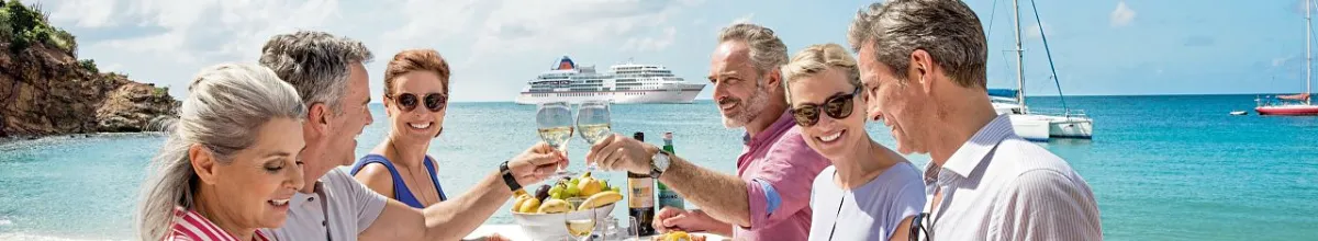Stammgäste genießen exklusive Momente bei einem Glas Wein am Strand vor einem Hapag-Lloyd Cruises Schiff.