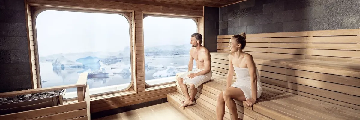 Hapag-Lloyd Cruises Club – Exklusive Entspannung im Spa mit Meerblick Gäste entspannen in der Panoramasauna eines HANSEATIC-Expeditionsschiffs von Hapag-Lloyd Cruises mit Blick auf arktische Eisberge.